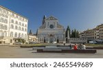 Basilica of Santa Maria Novella front view in the homonym square timelapse hyperlapse in Florence. Flowerbeds and green grass. People sitting on a bench. Blue sky at summer day