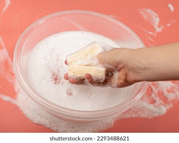 A Basin with Soapy Water, Hand Holds Soapy Sponge with Foam on Pink Background, Copy Space - Powered by Shutterstock