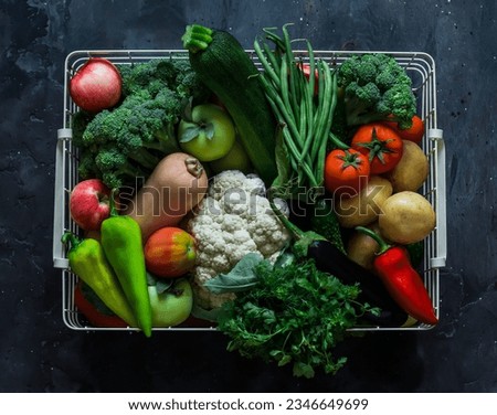 A basket with an abundant autumn seasonal harvest of vegetables - pumpkin, cauliflower, broccoli, string beans, squash, potatoes, tomatoes on a dark background, top view  