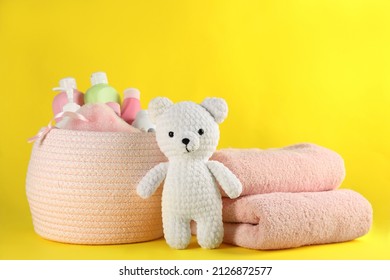 Basket With Baby Cosmetic Products, Toy Bear And Towels On Yellow Background