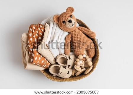 Basket with baby stuff and accessories for newborn. Gift basket with cotton clothes and muslin swaddle blanket, baby shoes, toys and cute teddy bear in beige colors. 