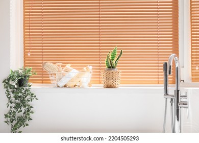 Basket With Bath Accessories And Houseplants Near Window In Bathroom