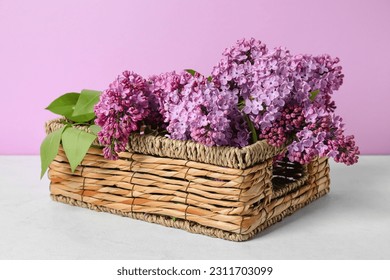 Basket with blooming lilac branches on table against pink background - Powered by Shutterstock