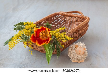 Basket with a bouquet of mimosa and tulips next to the toy sheep (mass production products)