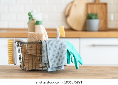 Basket with brushes, rags, natural sponges and cleaning products. Modern kitchen interior in the background. House cleaning concept