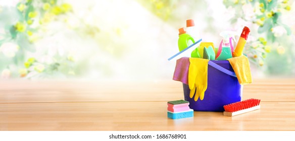 Basket With Cleaning Items On Wooden Table And Fresh Blurry Spring Flowers In Background.