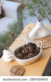 Basket with coniferous cones and pine tree branches on table in living room