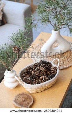 Basket with coniferous cones and pine tree branches on table in living room