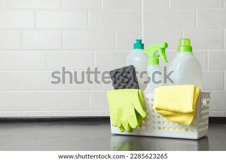 Basket with detergents, gloves and sponges on kitchen table. Harmless dishwashing detergent. Detergent for washing floors. Household cleaning chemicals. Chemical substances