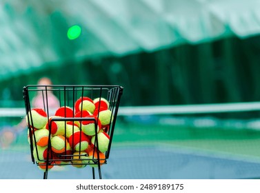 Basket filled with colorful beginner tennis balls on a tennis court. Horizontal photo. - Powered by Shutterstock