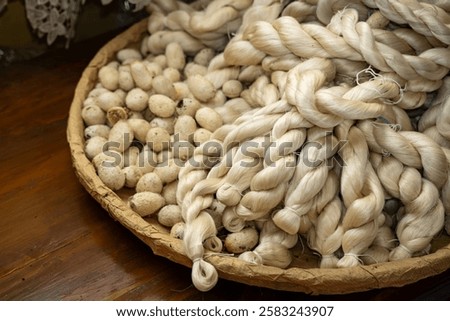 A basket filled with delicate silk threads intertwined with silkworm cocoons. The natural textures and colors highlight the artisanal quality. Ideal for textile and craft-related themes