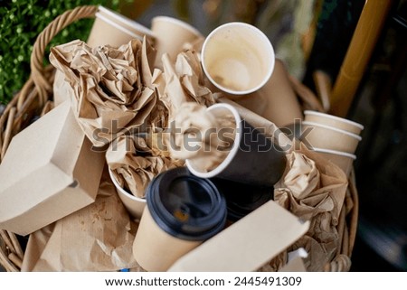 Basket filled with garbage with disposable tableware, top view. Cardboard beverage cups with plastic lids, fast food packaging, used napkins, copy space