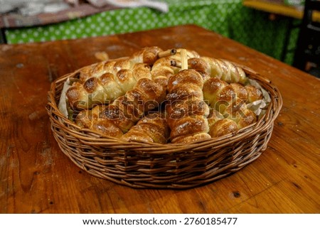 A basket filled with warm bread rolls sits on a wooden table at a busy market. People are chatting nearby as they enjoy the evening ambiance and local food.