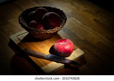 A basket with flat peaches in deep shadow  A basket with flat peaches and a knife on a wooden board 
