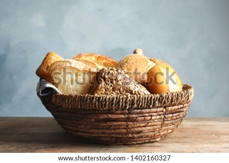 Basket with fresh bread on table against color background