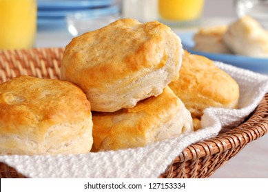 Basket of freshly baked biscuits with orange juice and tableware in background.  Closeup with shallow dof.