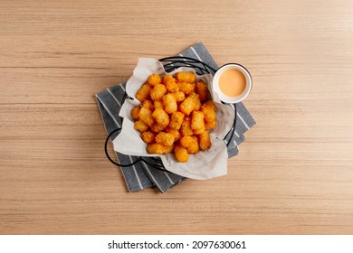 A basket of fried tater tots topped, on a rustic wooden counter - Shutterstock ID 2097630061