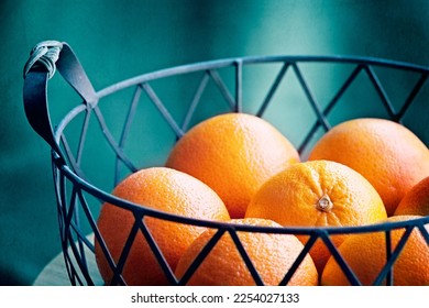 A basket of oranges against a teal background.  Fruit still life photography in turquoise.