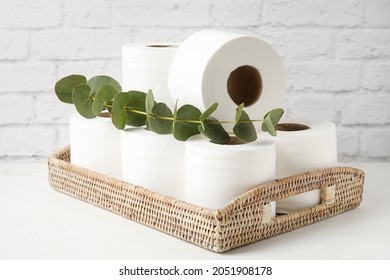 Basket with rolls of toilet paper and eucalyptus on table near brick wall