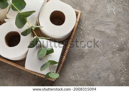 Basket with rolls of toilet paper and eucalyptus branch on grunge background