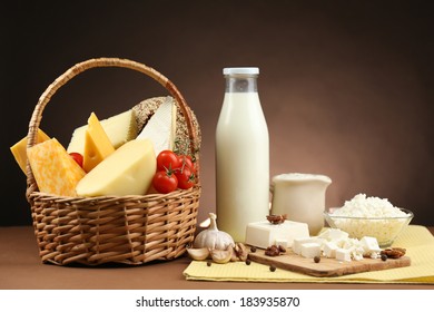 Basket With Tasty Dairy Products On Wooden Table, On Dark Brown Background