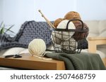 Basket with yarns, knitting needles, scissors and sweater on wooden table indoors