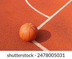 Basketball ball on the ground. Close-up ball on the red court. Basketball on the street or indoor court. Sports gear without people. Minimalism. Template, sport background 