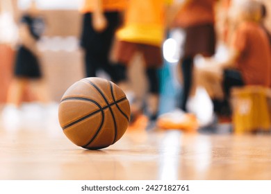 Basketball Ball On Hardwood Floor Youth Basketball Team in Background. Indoor Sports Training Unit for School Kids - Powered by Shutterstock