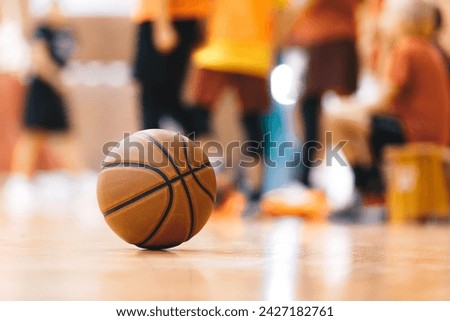 Basketball Ball On Hardwood Floor Youth Basketball Team in Background. Indoor Sports Training Unit for School Kids