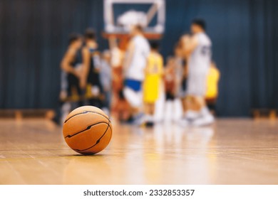 Basketball ball on wooden court. Young boys play basketball match in blurred background. Junior level sports team compete in indoor game - Powered by Shutterstock