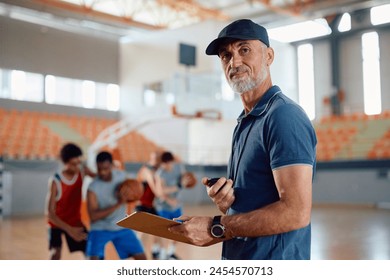 Basketball coach during sports training looking at camera. His players are in the background. Copy space. - Powered by Shutterstock