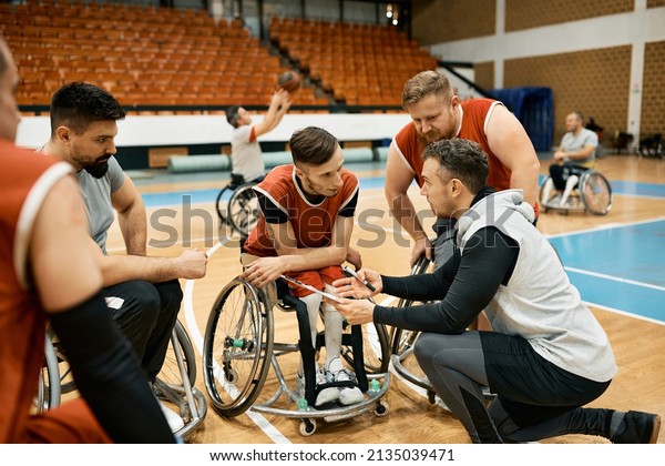 Basketball coach explaining\
the game plan to his team during wheelchair basketball sports\
training.