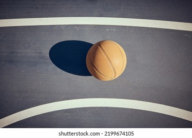 Basketball, Empty Game Court And Sports Ball Ready For Sport Exercise And Health Training. Top View Of Orange Workout Fitness Tool For Fun Team Sport With A Light Shining Casting A Shadow On A Floor