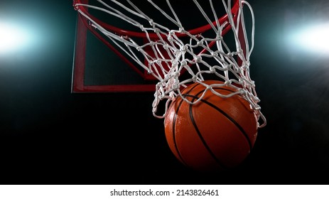 Basketball going through the basket on black backgorund, detail shot.