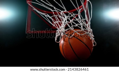 Basketball going through the basket on black backgorund, detail shot.