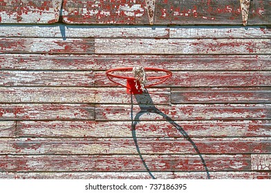 basketball hoop attached to weathered barn wall covered with crazed and peeling red and white paint