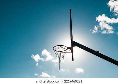 A basketball hoop backlit by the sun with a summer blue sky forming a contour, sillhouette
