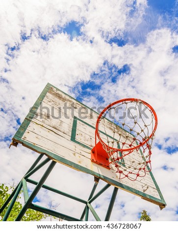 Basketball hoop in the park against white clouds and blue sky.
