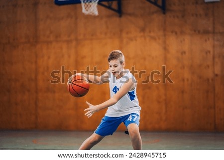 A basketball kid in action dribbling a ball on court during a training. A junior basketball player is dribbling a ball on basketball court. Dynamic picture of a junior athlete in action with a ball.