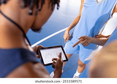 Basketball male coach using tablet to discuss game strategy with female players. Sports, coaching, teamwork, technology, training - Powered by Shutterstock