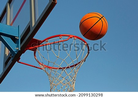 A basketball in a net on a blue sky background. The ball hit the ring. Sports, team game. Conceptual: victory, success, hitting the target, sport. 