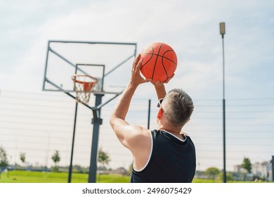 A basketball player aiming a shot towards the hoop, captured from behind, on an outdoor court.

 - Powered by Shutterstock