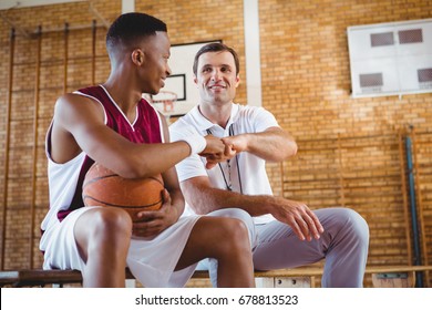 Basketball player doing fist bump with coach while sitting on bench in court - Powered by Shutterstock