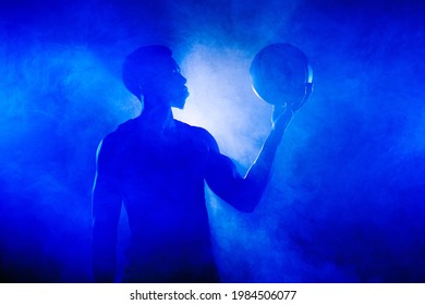 Basketball player holding a ball against blue fog background. African american man silhouette. - Powered by Shutterstock