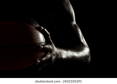 Basketball player holding a ball against black background. Abstract wet male body of african american man. Muscular person sidelit silhouette. - Powered by Shutterstock