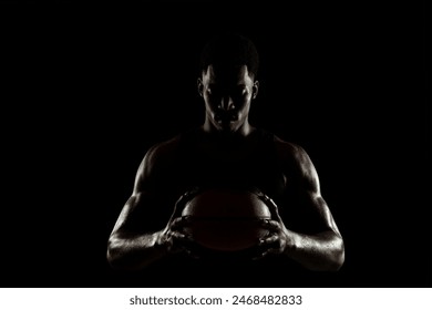 Basketball player holding a ball against black background. Serious concentrated african american man. Muscular person sidelit silhouette. - Powered by Shutterstock