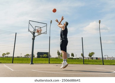 A basketball player jumps to shoot the ball towards the hoop on an outdoor court, showcasing focus and skill on a sunny day. - Powered by Shutterstock