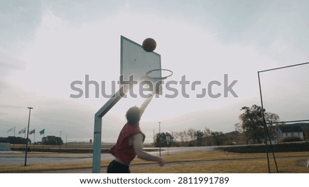 Basketball player performs a slam dunk. Performing slam dunk tricks. Street basketball. Basketball going through the basket with Sky in the background.