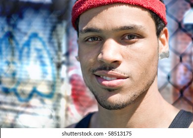 A basketball player posing at the park outdoors in front of a chain linked fence and some grafitti.