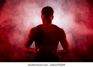 Basketball player side lit with red color holding a ball against smoke background. Serious concentrated african american man. - Powered by Shutterstock